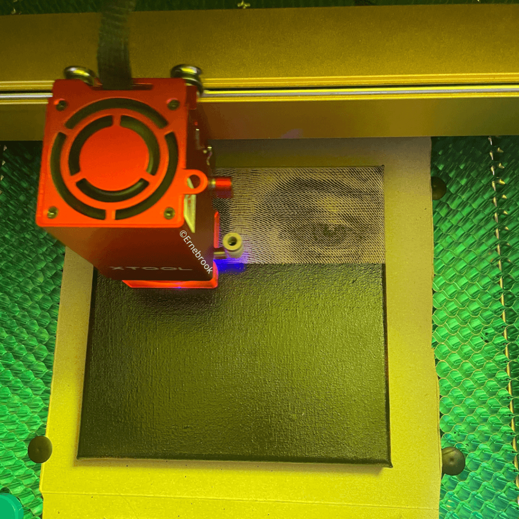 A red laser machine engraving a black canvas with the image of a face with closed eyes.