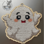 A white friendly ghost cross-stitch home decoration. Cut out of 3mm plywood with a cross-stitch design embroidered on a silver background.