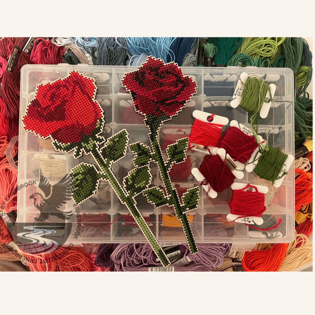 A straight stem and a right-facing single stem rose in cross-stitch with a selection of embroidery threads.
