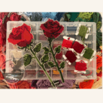 A straight stem and a right-facing single stem rose in cross-stitch with a selection of embroidery threads.