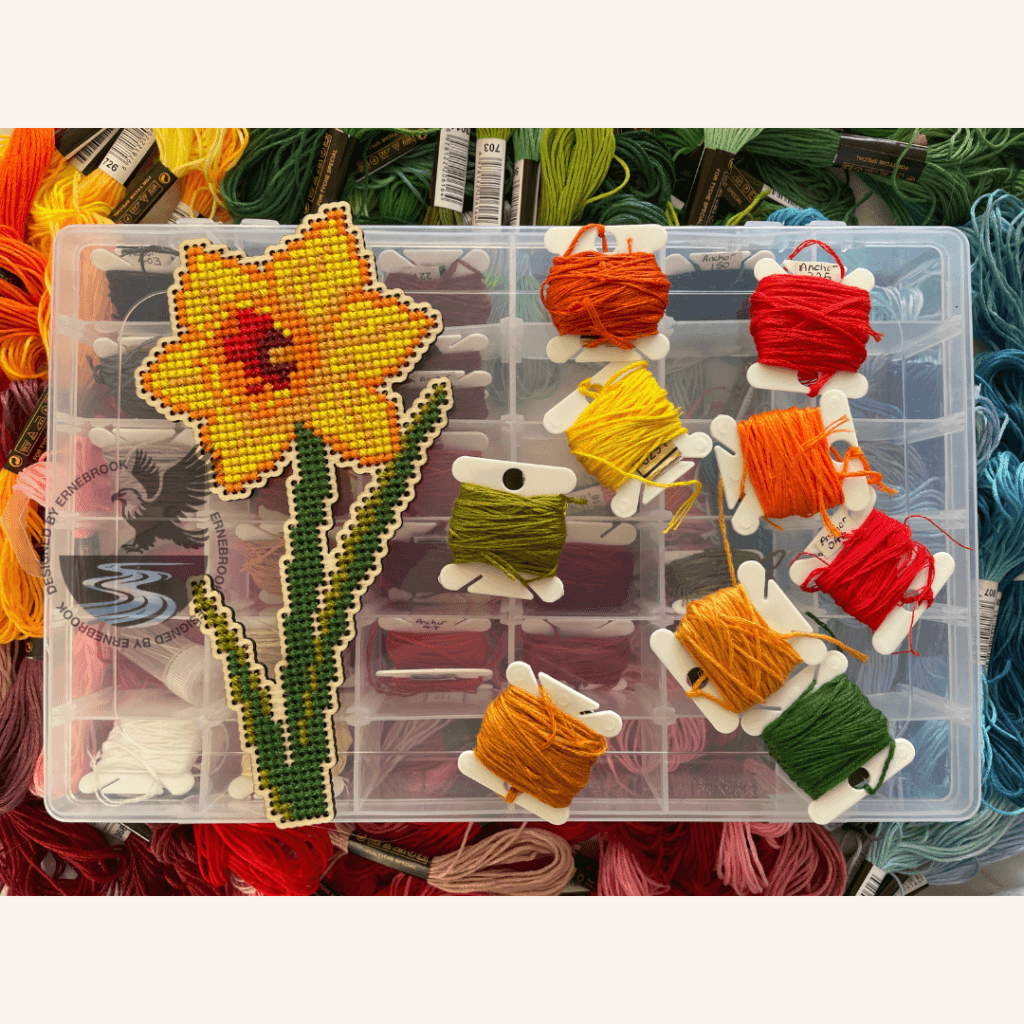 A completed single daffodil cross-stitch project with a selection of embroidery threads.