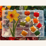 A completed single daffodil cross-stitch project with a selection of embroidery threads.