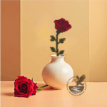 Image of a single red rose template in wood and completed with cross stitch embroidery in a white vase. A real red rose is laying to the side.