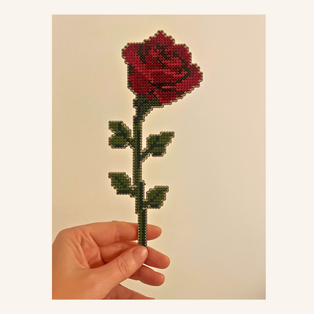 An elegant cross-stitch home decoration. Cut out of 3mm plywood with a cross-stitch design embroidered and being heldupright between thrumb and finger