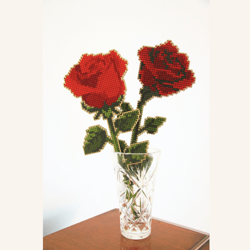Image of two red rose templates in wood and completed with cross stitch embroidery in a small glass vase.