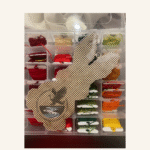 An uncompleted cross-stitch project of an Easter bunny with a selection of embroidery threads.
